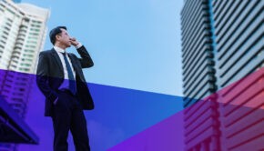 Businessman on a cellphone looking up at a skyscraper